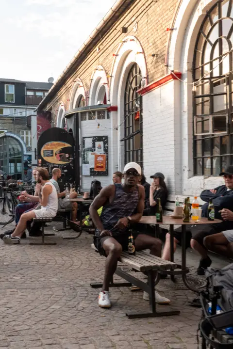 Drinkers at tables on the cobbles in front of tall arched windows, Christiania, Copenhagen