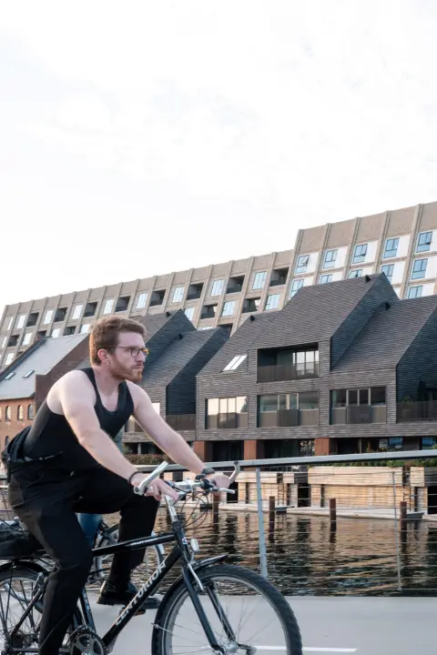 A cyclist in a tank top passing new buildings with pointed roofs, Copenhagen