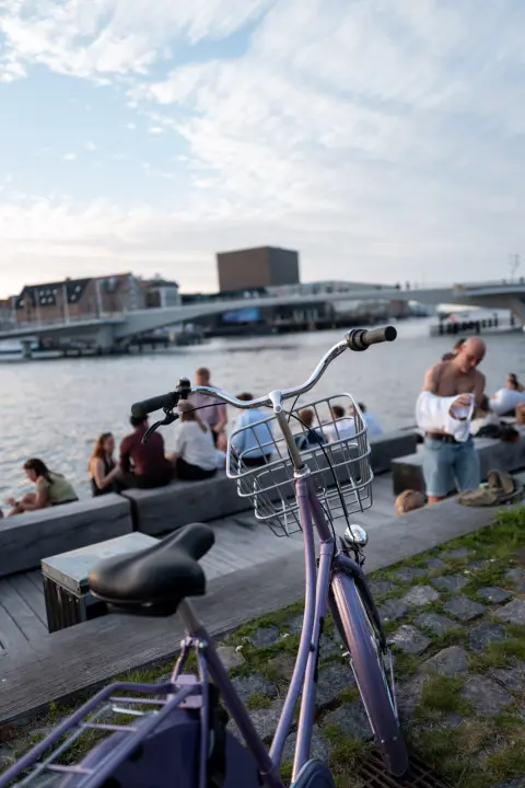 A bicycle parked by the harbour, people sitting facing the water, Copenhagen