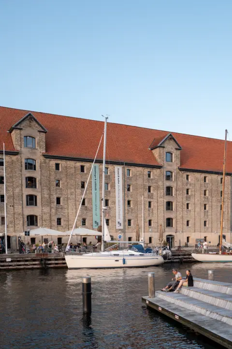 A large warehouse with a red roof and a sailboat in the evening light, Copenhagen