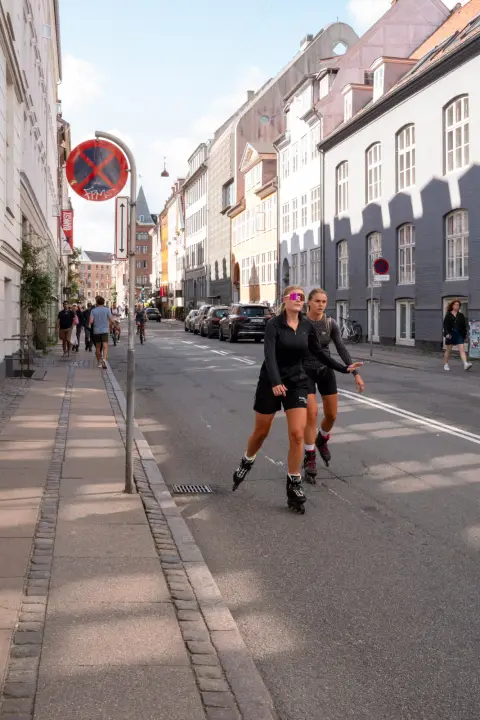 Two young women on rollerblades coming down a sunny street, Copenhagen