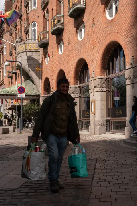 A man carrying shopping bags under brick arcades, Copenhagen