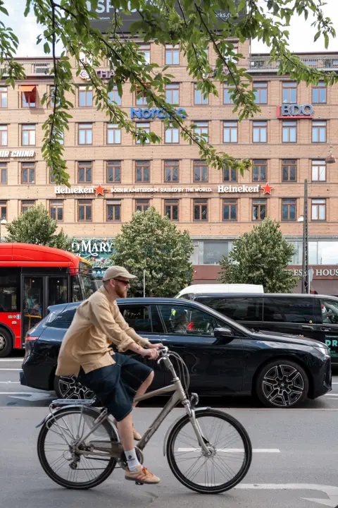 A cyclist in a beige jacket passing a red bus, Copenhagen
