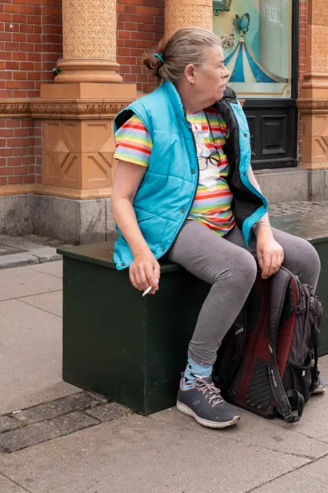 A woman in a turquoise vest smoking, sitting on a box, Copenhagen
