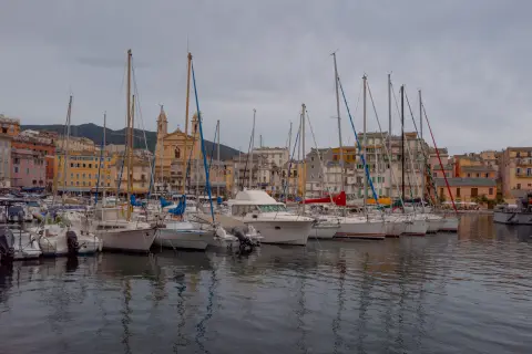 Voiliers amarrés devant les façades colorées d’un vieux port, un soir nuageux, Corse