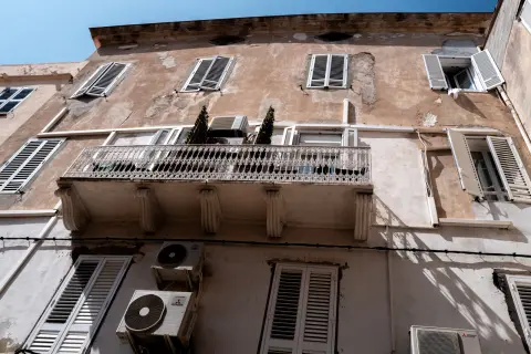 Façade décrépie aux volets blancs et balcon en fer forgé, en contre-plongée, Calvi, Corse