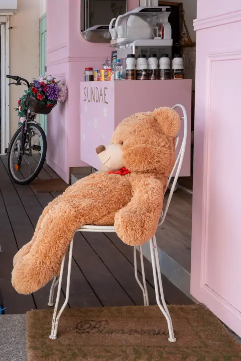 Un grand ours en peluche assis sur une chaise devant un glacier, Calvi, Corse