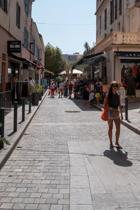 Une passante au chapeau de paille remonte une rue pavée en plein soleil, Calvi, Corse