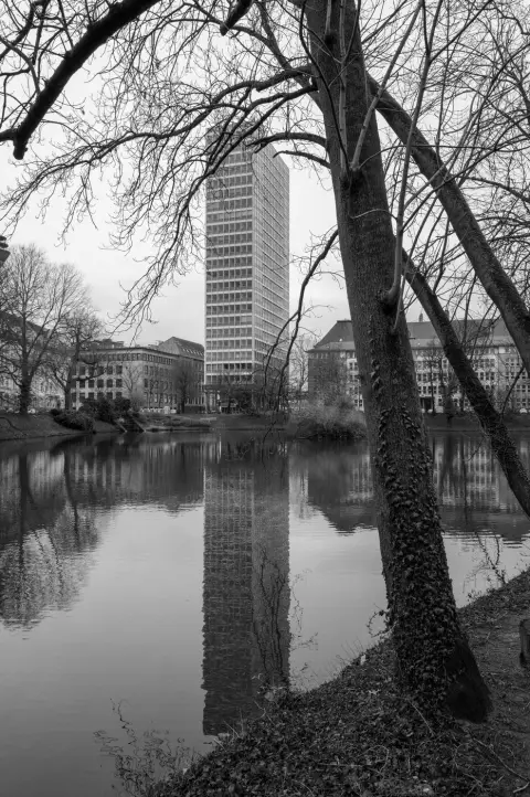 Une tour vitree elancee se refletant dans un plan d'eau borde d'arbres, Düsseldorf
