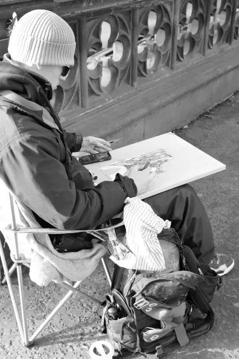 Sketch artist on a folding stool, drawing board on his knees, below a Gothic balustrade, Edinburgh