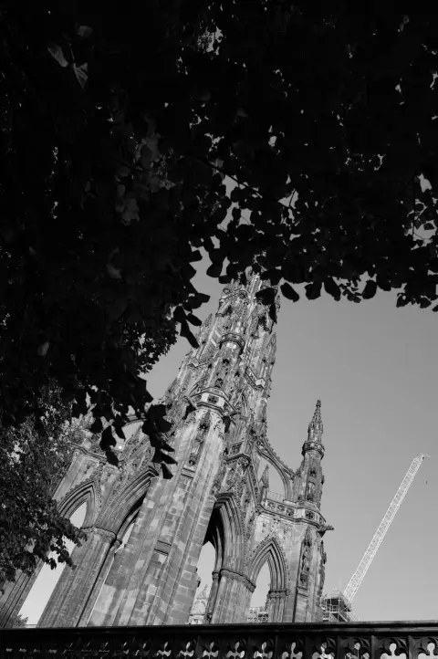 Spire of the Scott Monument framed by leaves, a crane in the distance, Edinburgh