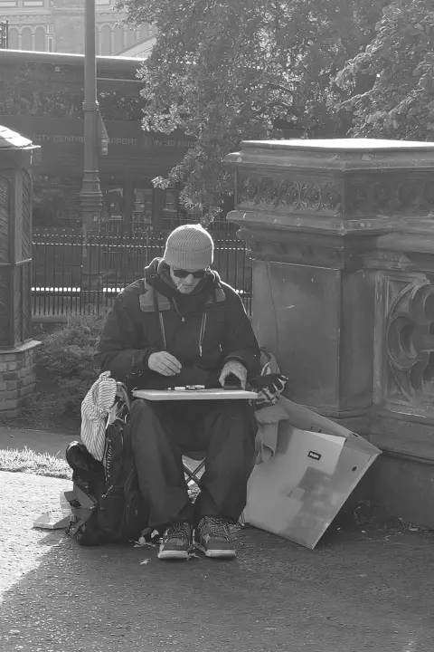 Sketch artist sitting on the pavement, drawing board on his lap, Edinburgh