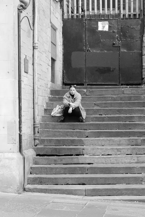 Young woman sitting alone on steps in front of an iron door, Edinburgh