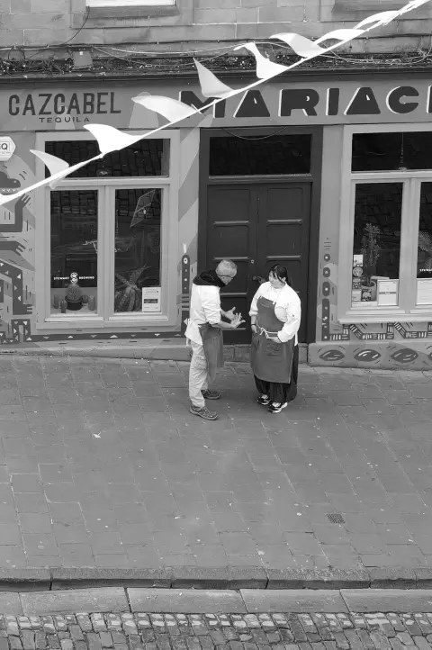Two people talking in front of a colourful shopfront, bunting overhead, Edinburgh