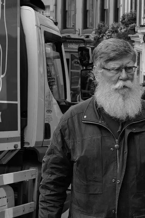 Man with a long white beard walking past a lorry, Edinburgh