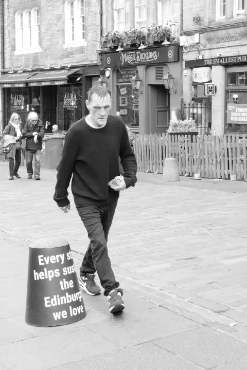 Man crossing a pedestrian square lined with pubs, Edinburgh