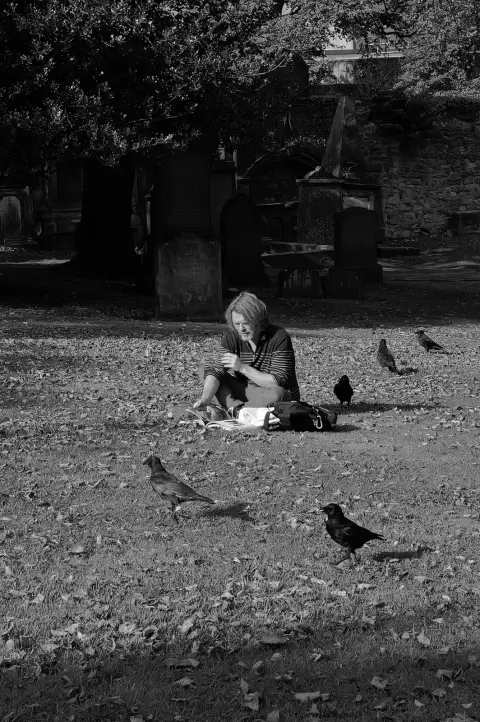 Woman sitting on the grass of a graveyard among crows, Edinburgh