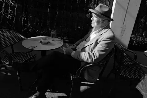 Man in a hat sitting at a café table in bright sunlight, Edinburgh