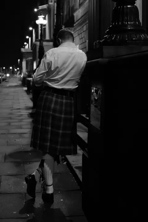 Man in a kilt leaning against a wall at night, Edinburgh