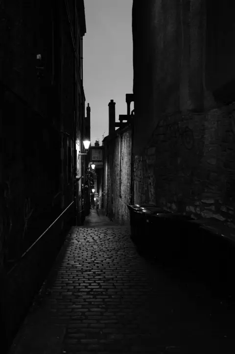 Cobbled lane between tall dark walls at nightfall, Edinburgh