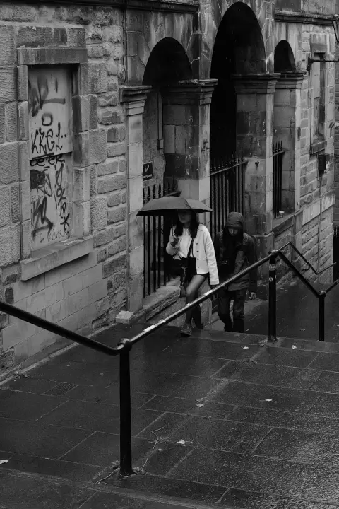 Woman under an umbrella coming down wet steps, Edinburgh