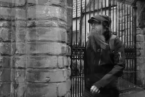 Bearded man in a cap walking past railings, Edinburgh