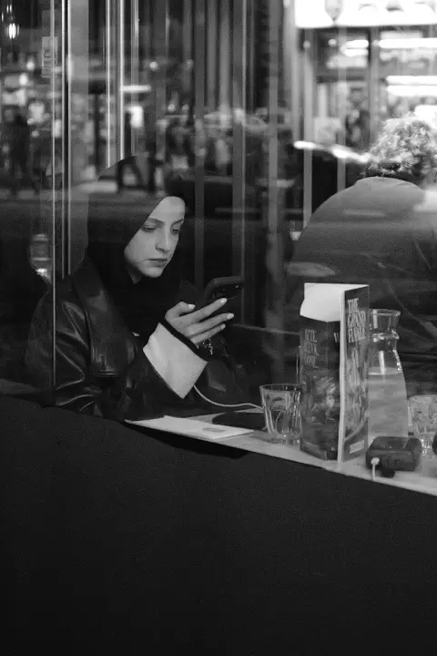 Young woman in a headscarf behind a café window, phone in hand, Edinburgh