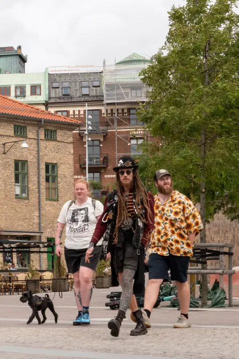 Three passers-by and a small black dog crossing a square, Gothenburg