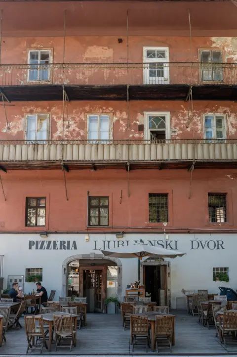 Terrasse de la Pizzeria Ljubljanski Dvor sous une facade rose fanee, Ljubljana