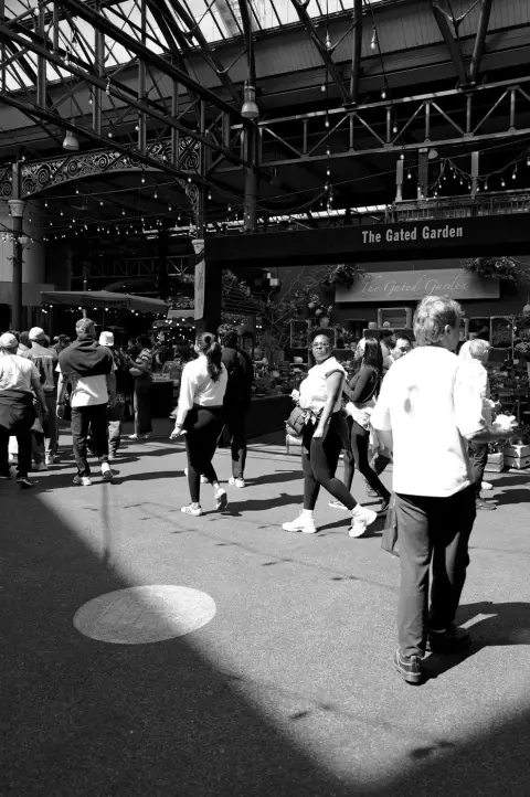 Foule de visiteurs déambulant sous la verrière d'une halle de marché couverte, Londres