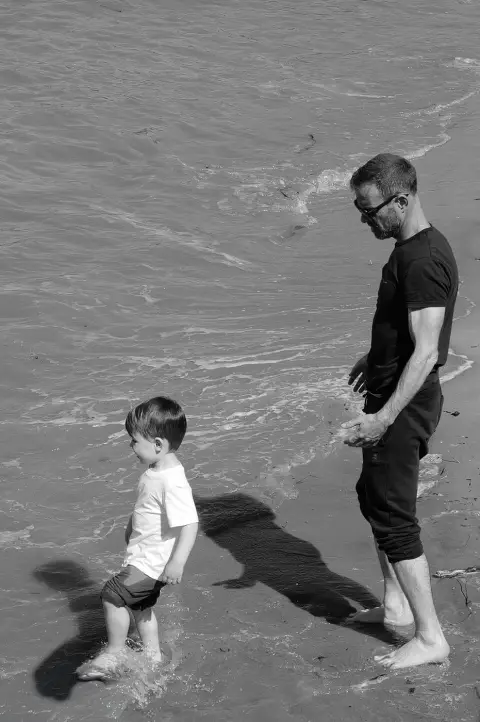 Un père observe son jeune fils patauger pieds nus dans les vagues, Londres