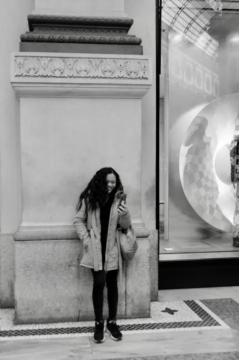 Jeune femme riant devant son téléphone, adossée à une colonne sculptée de la Galleria, Milan