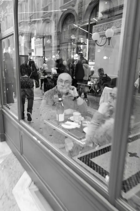 Reflet dans une vitrine d'un homme seul à une table de café, bouteille de vin devant lui, Milan