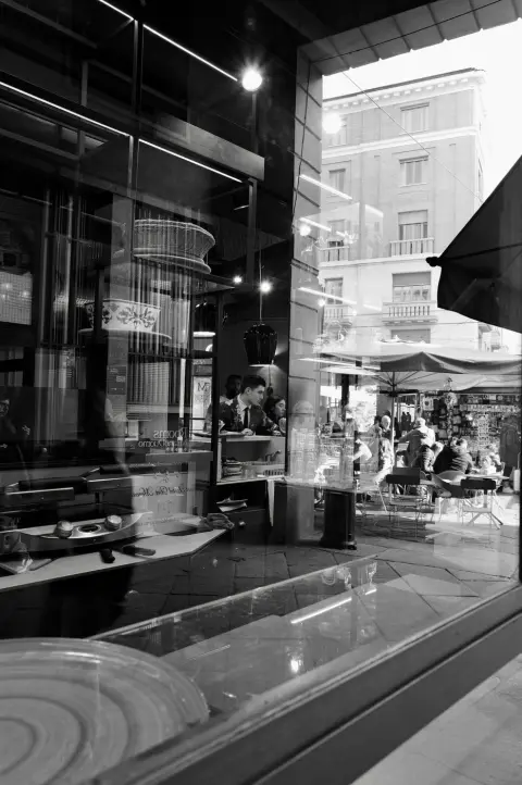 Reflet dans une vitrine d'une pâtisserie animée avec sa terrasse en plein air, Milan
