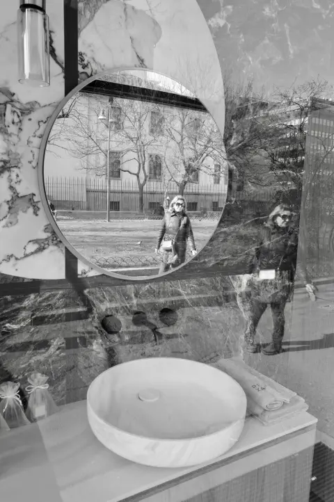 Miroir rond en vitrine reflétant une passante en blouson de cuir, Milan