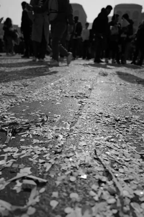 Confettis de carnaval jonchant les pavés, silhouettes de passants en arrière-plan, Milan
