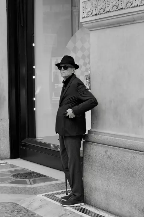 Homme élégant en chapeau et lunettes noires appuyé sur sa canne près d'une vitrine, Milan