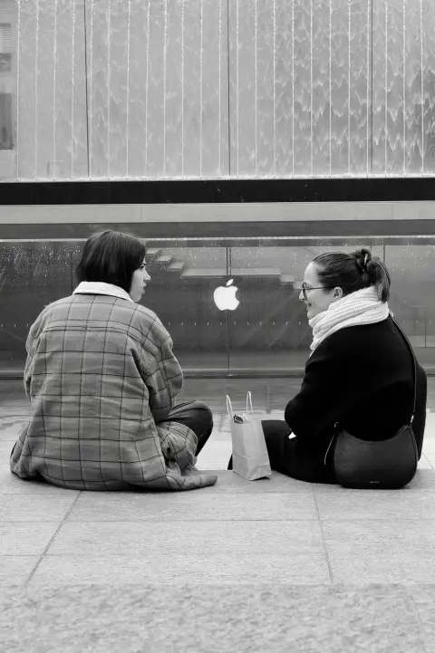 Deux amies assises dos à l'objectif devant le mur d'eau de la boutique Apple, Milan