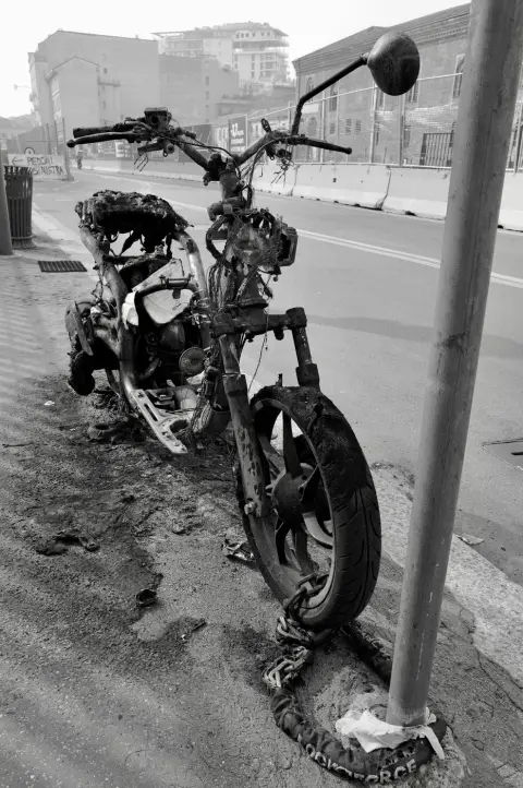 Carcasse calcinée d'un scooter enchaînée à un poteau au bord de la route, Milan