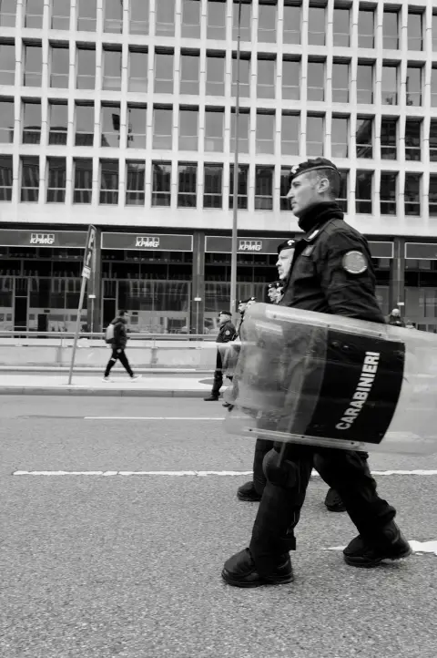 Carabinier en tenue anti-émeute, bouclier siglé en main, défilant devant un immeuble de bureaux, Milan
