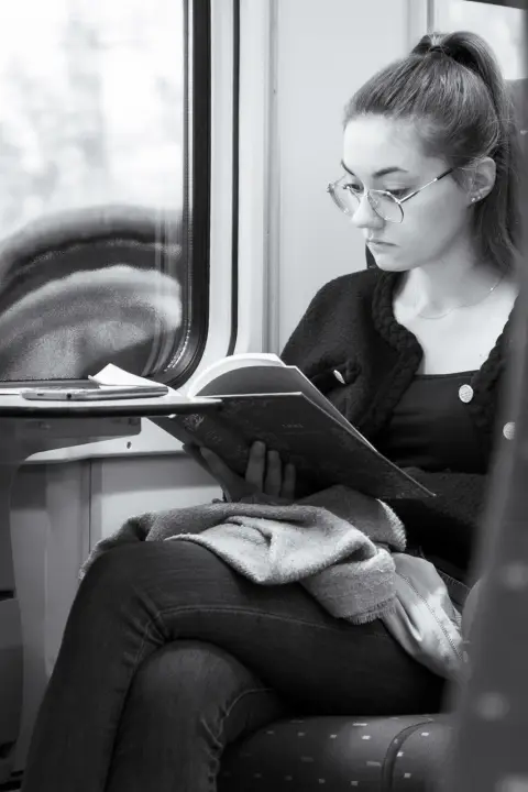 Une jeune femme lit, un crayon à la main, assise près de la fenêtre d’un train