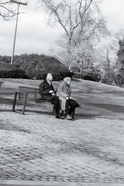Deux personnes âgées emmitouflées assises sur un banc dans un parc en hiver, Mons