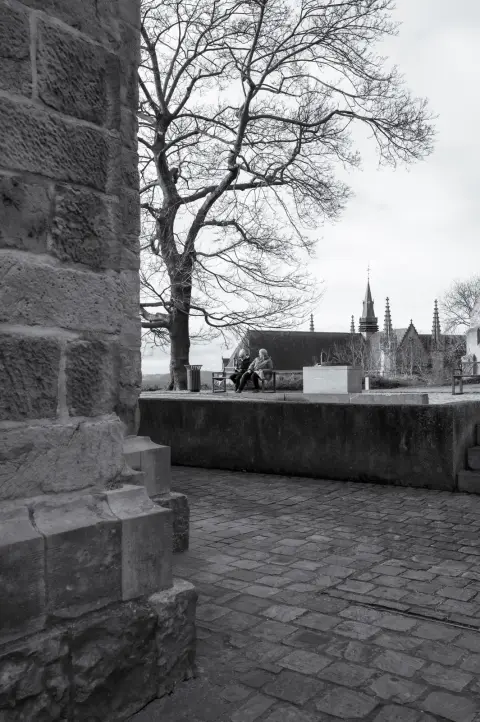 Une terrasse pavée sous les arbres nus, une flèche d’église au loin, Mons