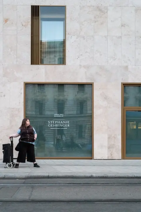 Une femme tire un chariot de courses devant une vitrine en marbre, Munich