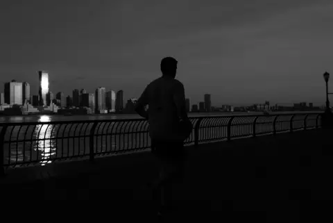 Coureur de dos au crépuscule face à la skyline reflétée sur l'eau, New York