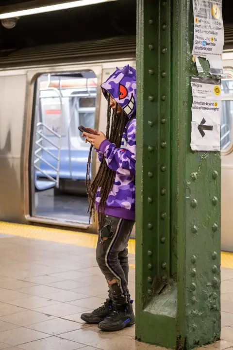 Adolescent en sweat imprimé monstre absorbé par son téléphone sur le quai, New York