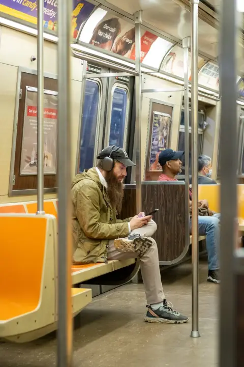 Homme barbu casqué assis dans le métro, absorbé par son téléphone, New York