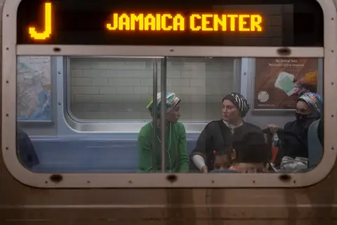 Passagères en foulard et un enfant vus à travers la vitre du train Jamaica Center, New York