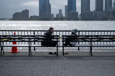 Couple assis dos à dos sur des bancs face au fleuve, skyline en fond, New York