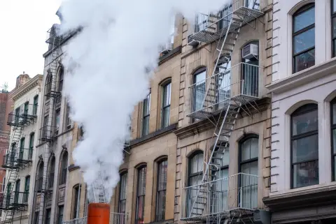 Vapeur s'élevant devant une façade aux échelles de secours, New York